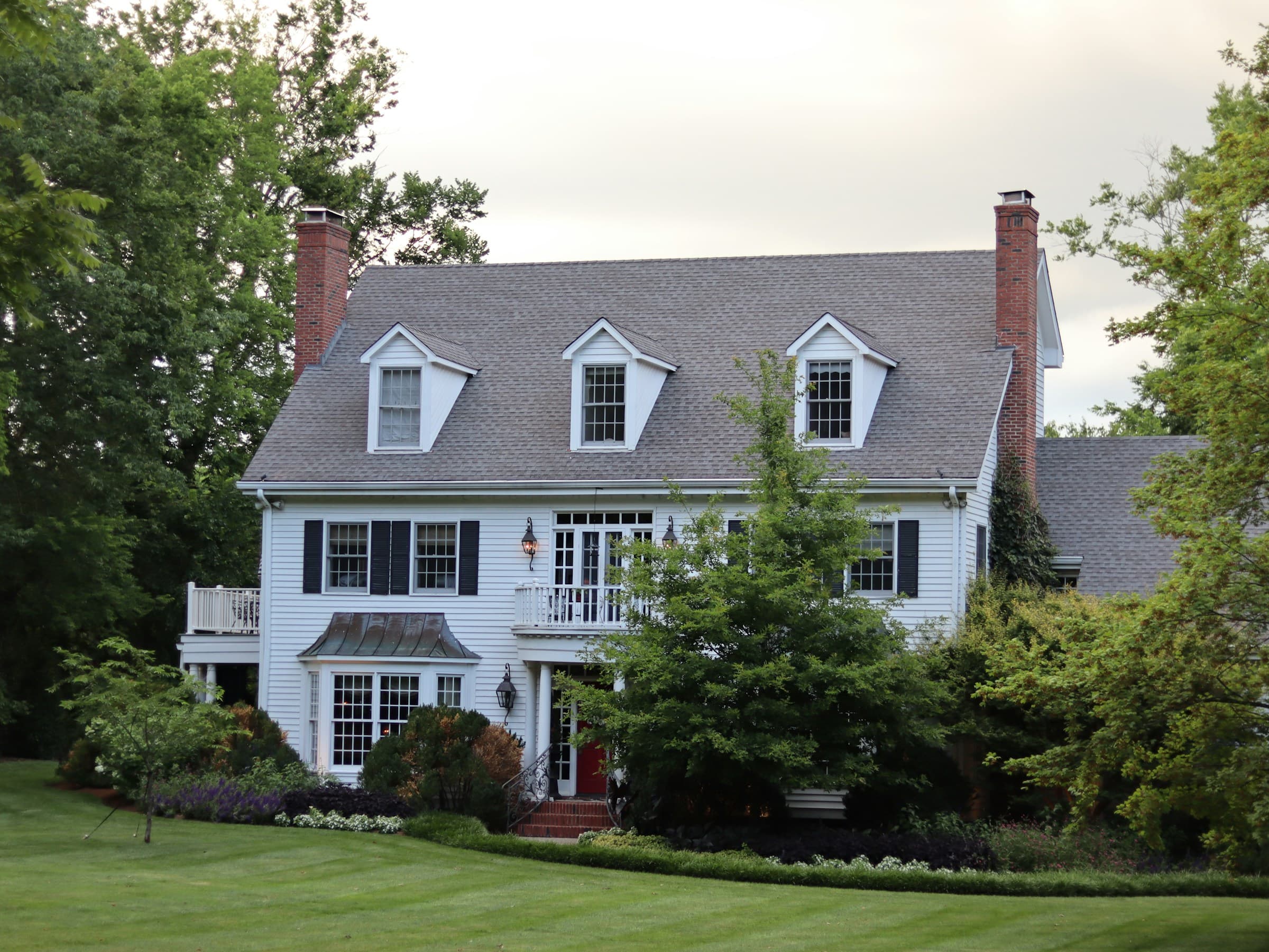 White colonial farmhouse with a gray shingle roof and three dormers
