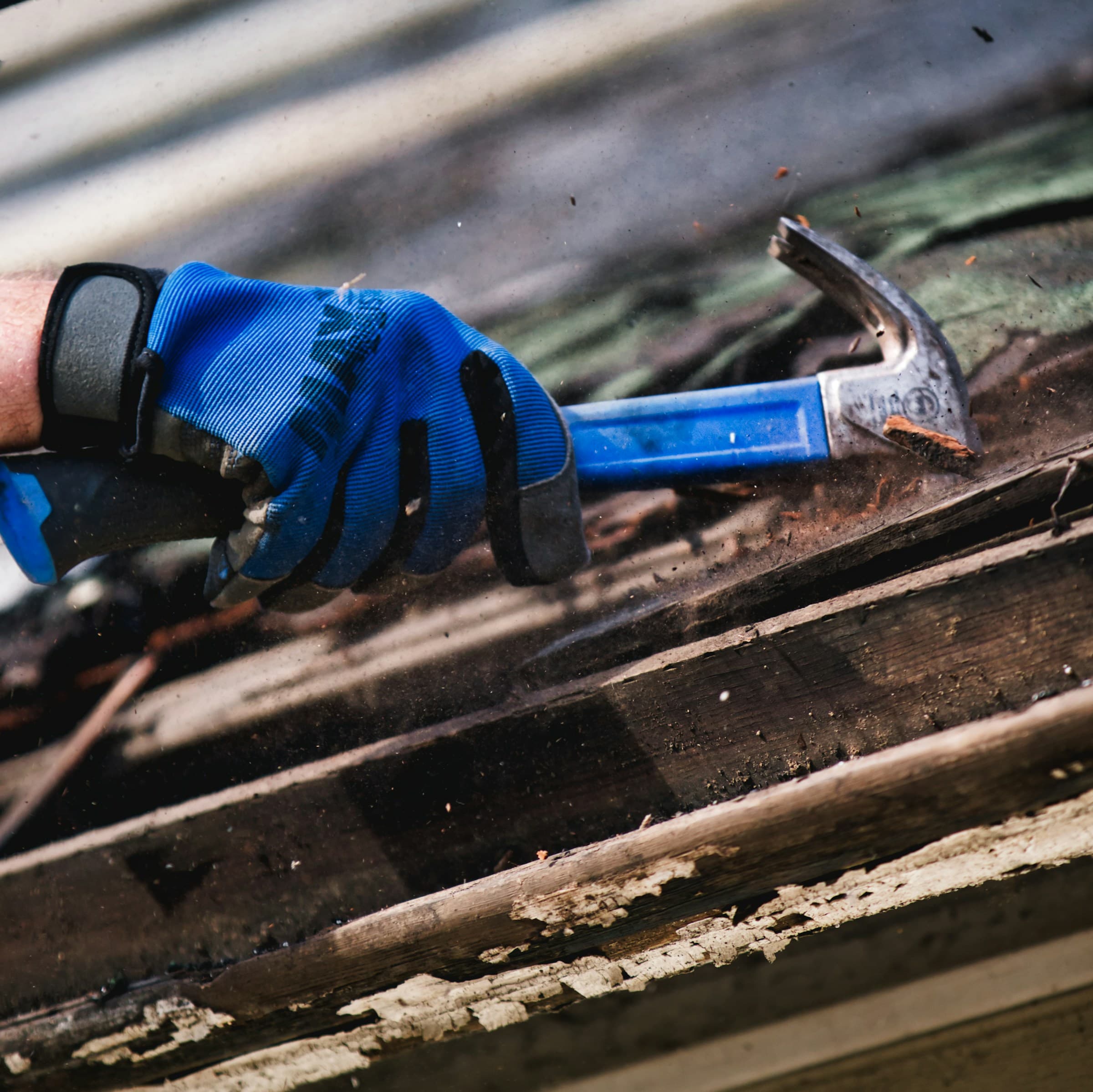 Gloved hand prying up old shingles with a hammer during a tear-off